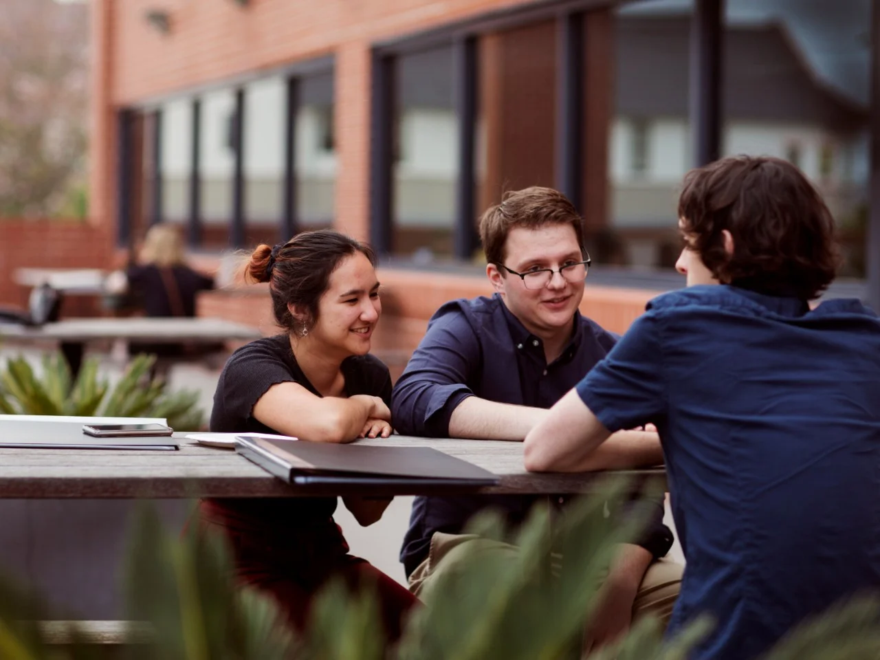 Group of three students sitting outdoors at a table Group of three students sitting outdoors at a table