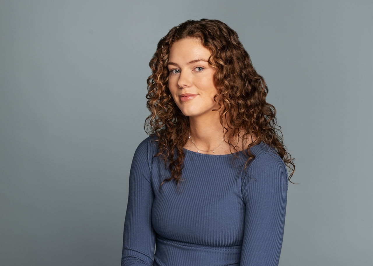 Female student with black shirt standing in front of brick wall.